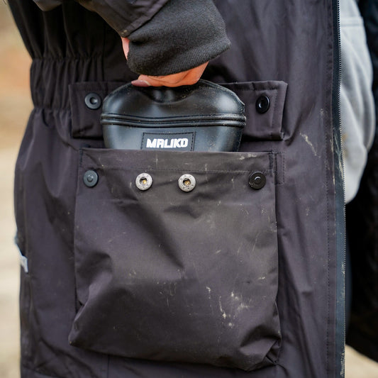 Person holding a black container labeled 'Maliko' in a dark jacket pocket.