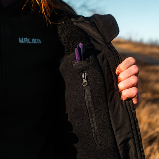 Person wearing a black maliko jacket with a visible brand logo, holding a purple item.