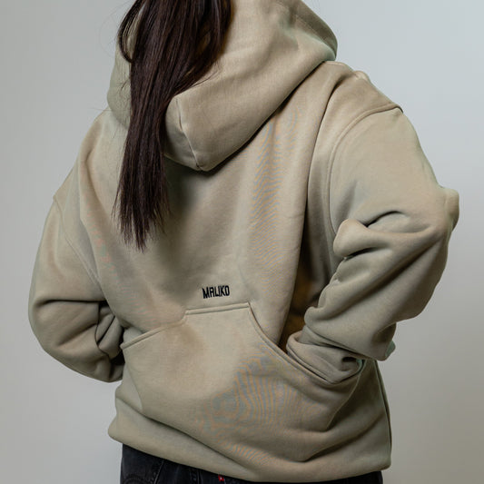 A person shown from the back wearing a light beige oversized dog training hoodie with a small black 'MALIKO' logo on the upper back