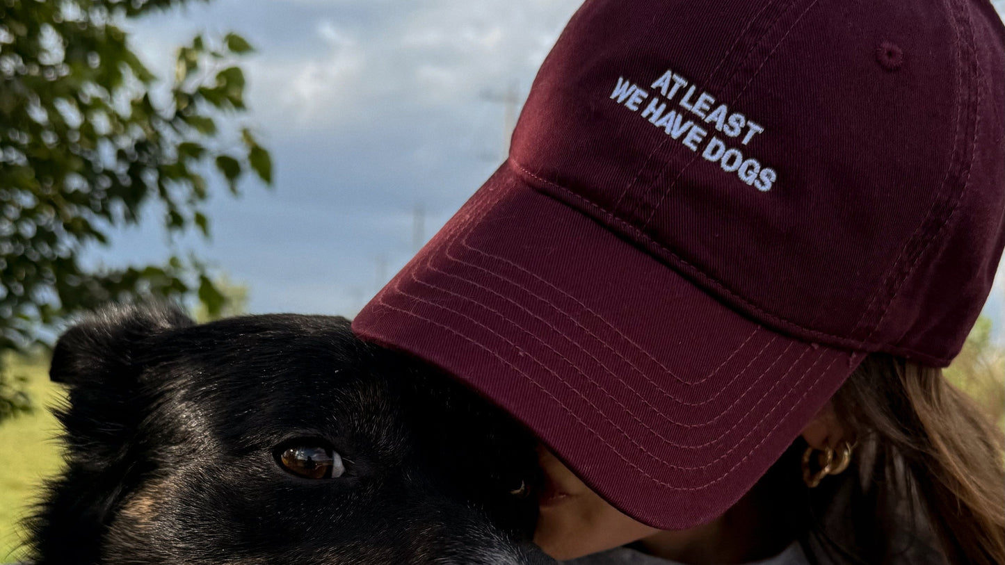 Person wearing a maroon cap with text and a dog outdoors