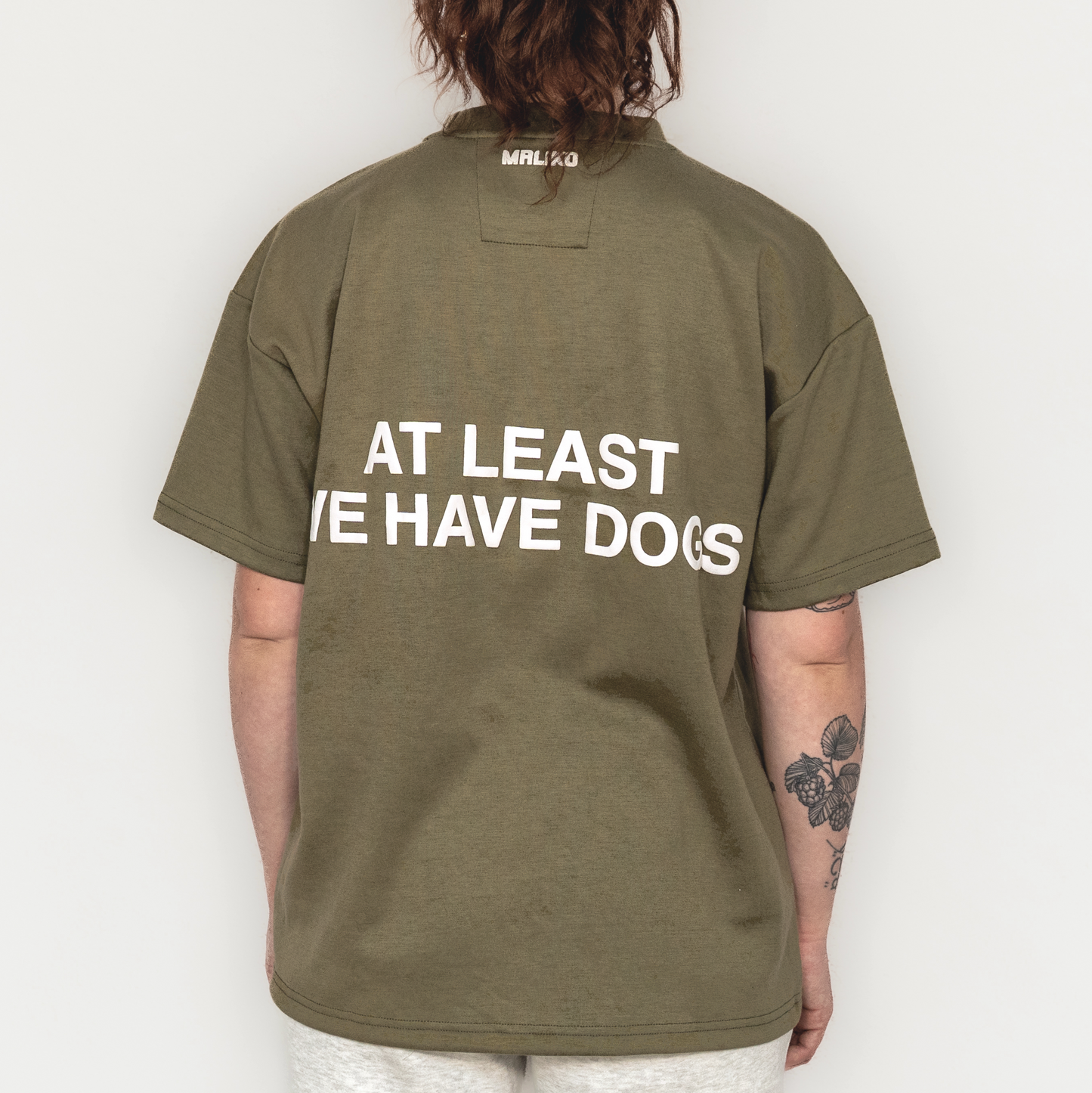Person wearing a green t-shirt with text on the back, standing against a plain background