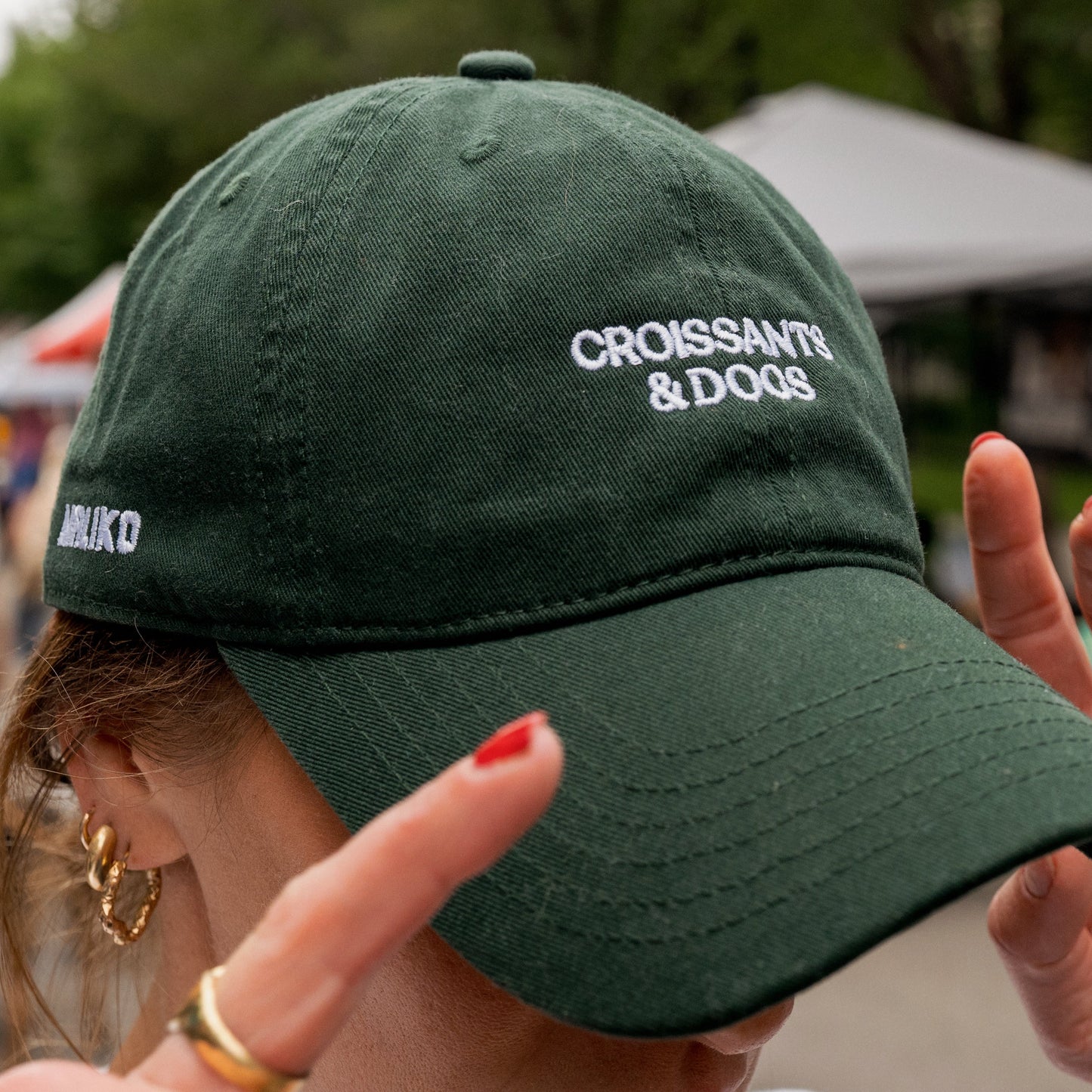 Person wearing a green cap with 'Croissants & Dogs' text, blurred outdoor background