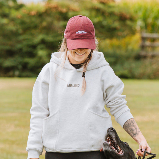 Woman in a white jacket and red cap standing with a large black dog on a grassy field.