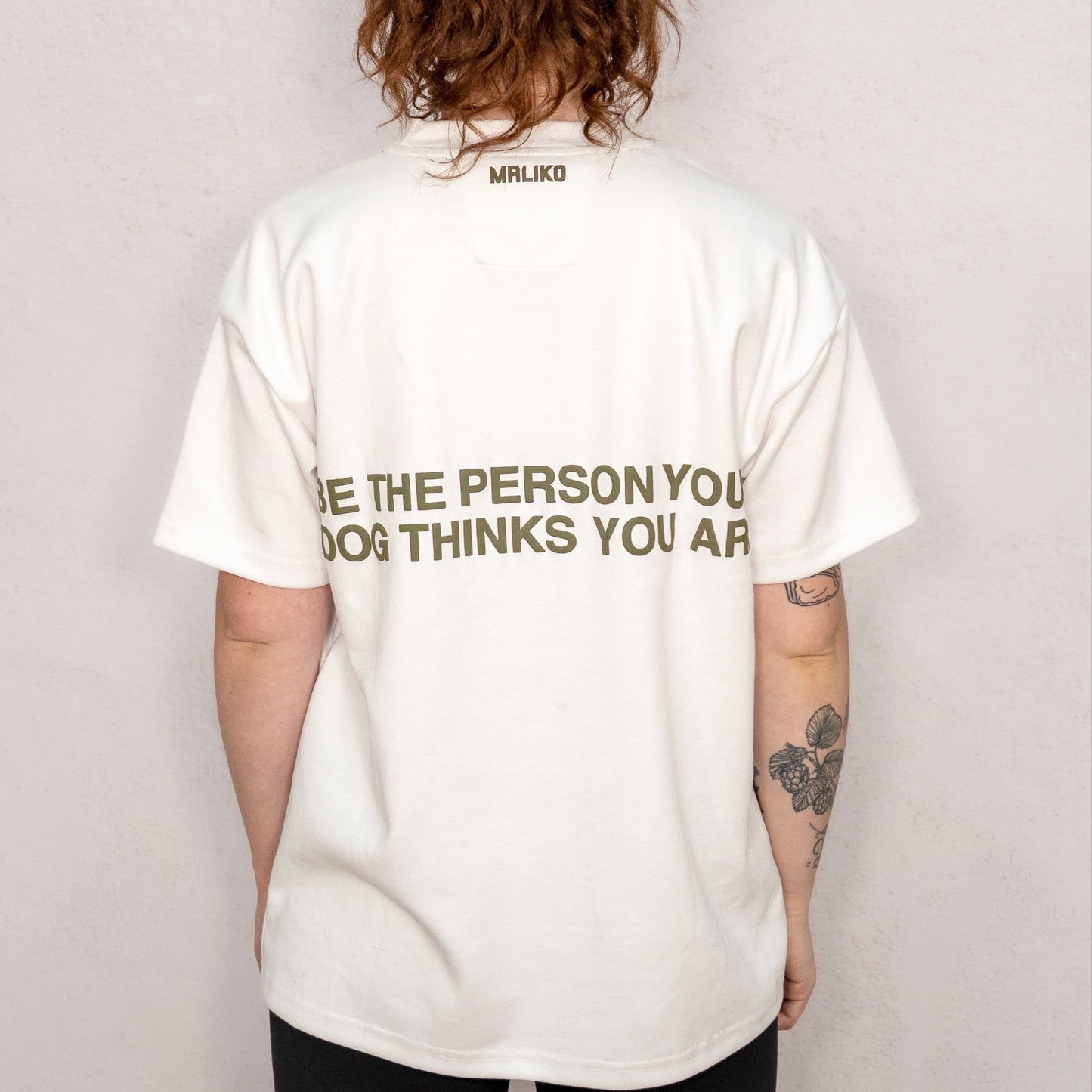 Person wearing a white t-shirt with text on the back, standing against a plain background