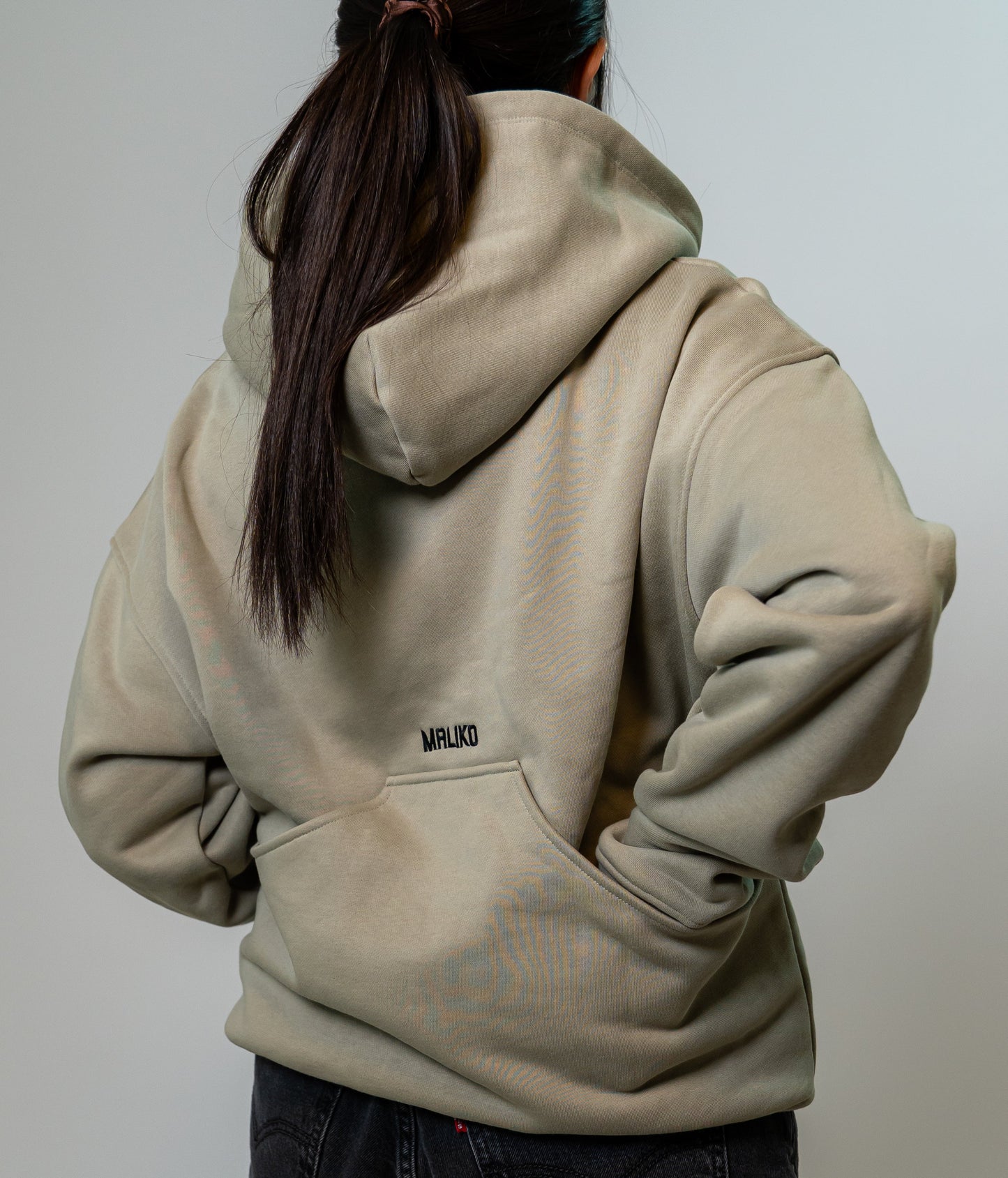 A person shown from the back wearing a light beige oversized dog training hoodie with a small black 'MALIKO' logo on the upper back