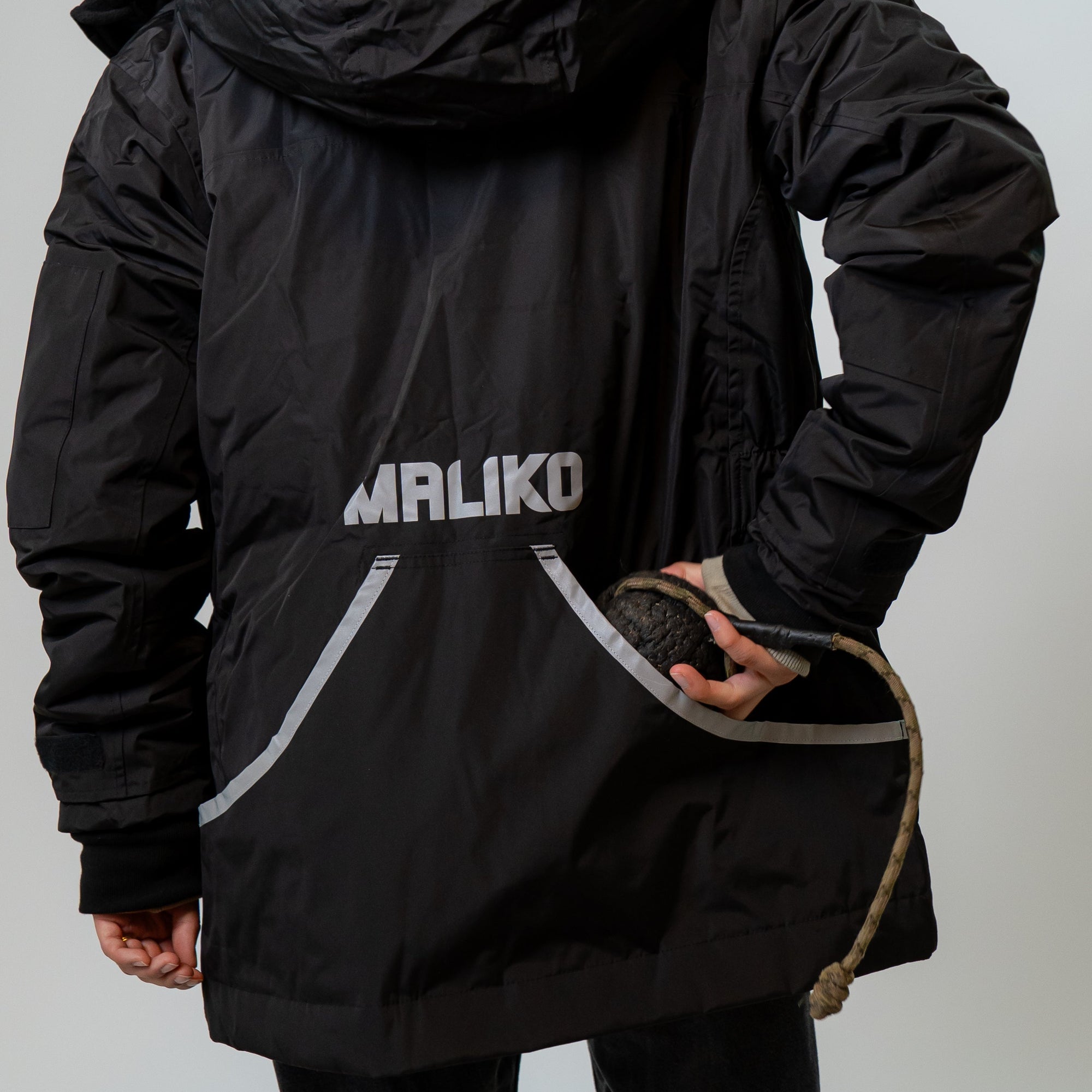 A person shown from behind wearing a black hooded jacket with a reflective 'MALIKO' logo printed on the back, against a plain light gray studio background