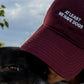 Person wearing a maroon cap with text and a dog outdoors