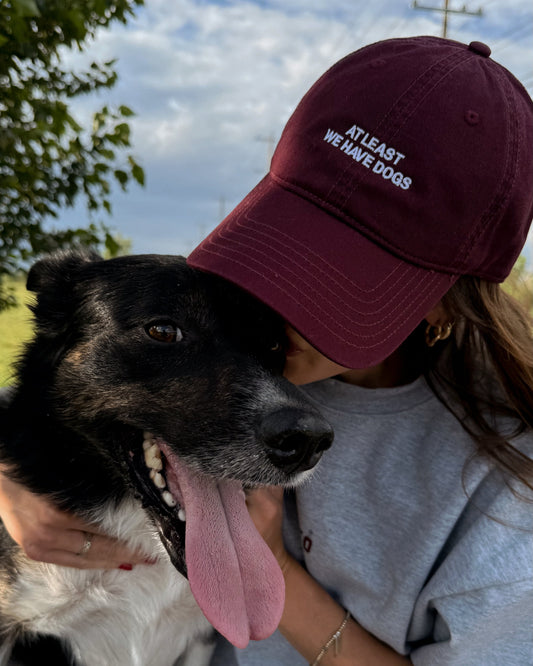 Person wearing a maroon cap with text and a dog outdoors