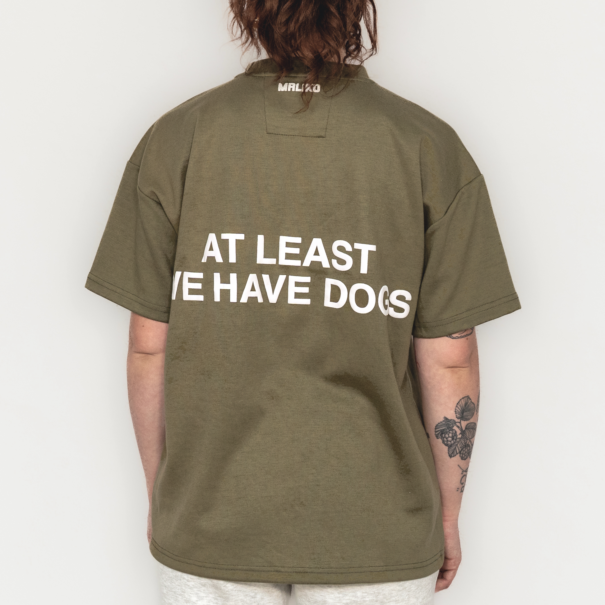 Person wearing a green t-shirt with text on the back, standing against a plain background
