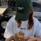 Person wearing a green cap and white t-shirt holding pastries with a truck in the background