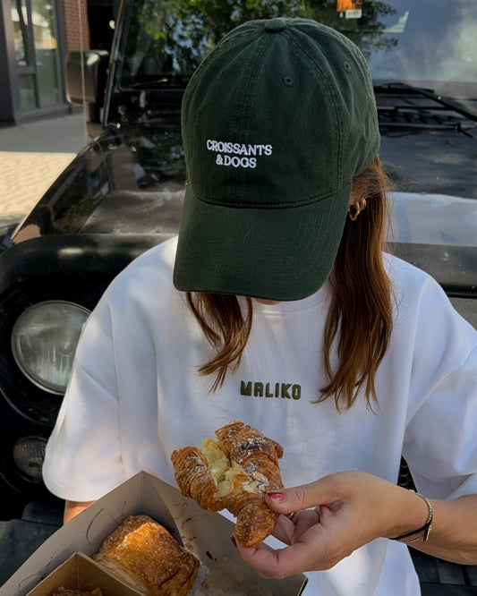 Person wearing a green cap and white t-shirt holding pastries with a truck in the background